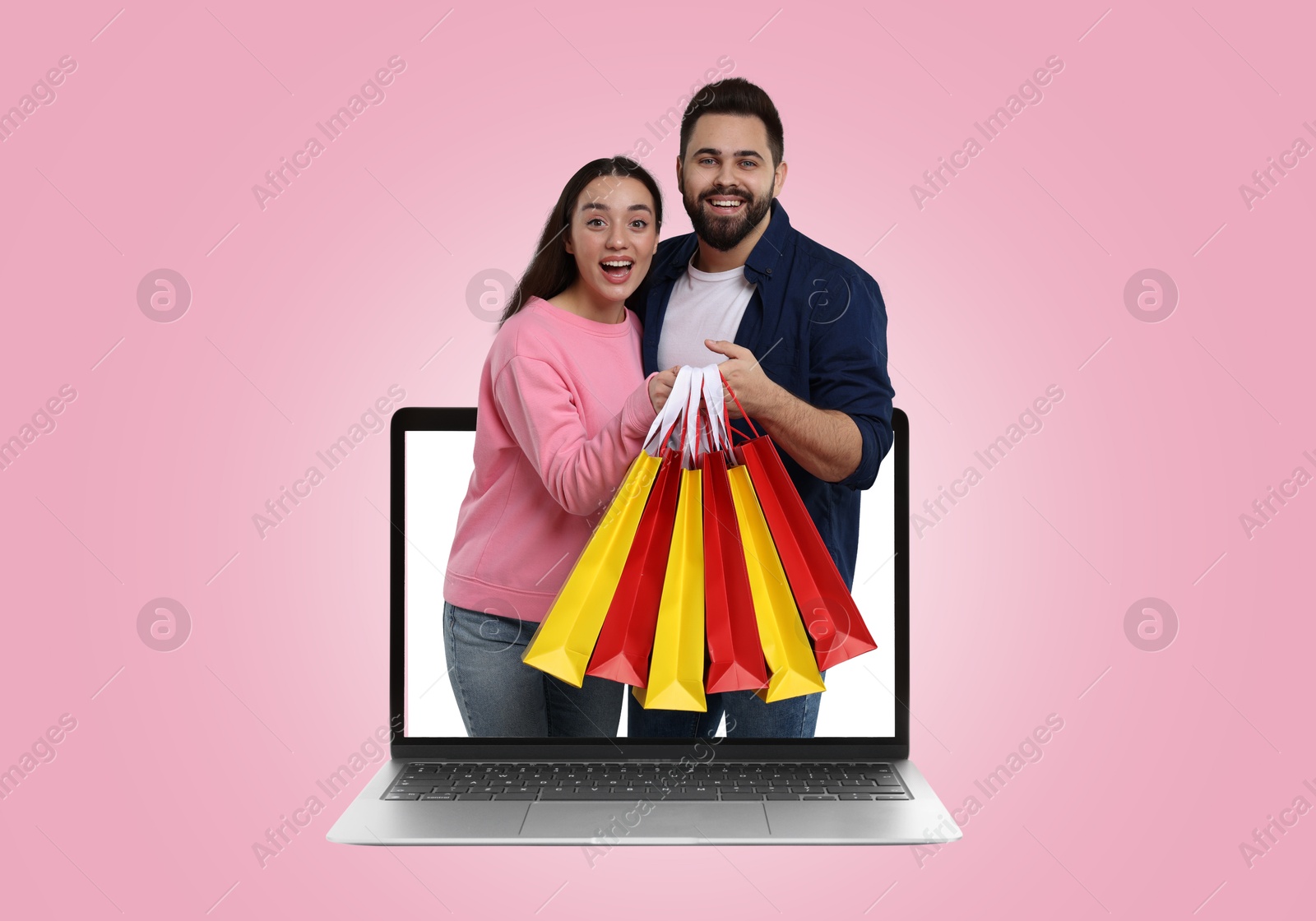 Image of Internet shopping. Happy couple with shopping bags coming out of laptop on pink background