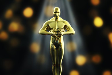 Image of Golden trophy in shape of human figure in light rays against black background with blurred lights