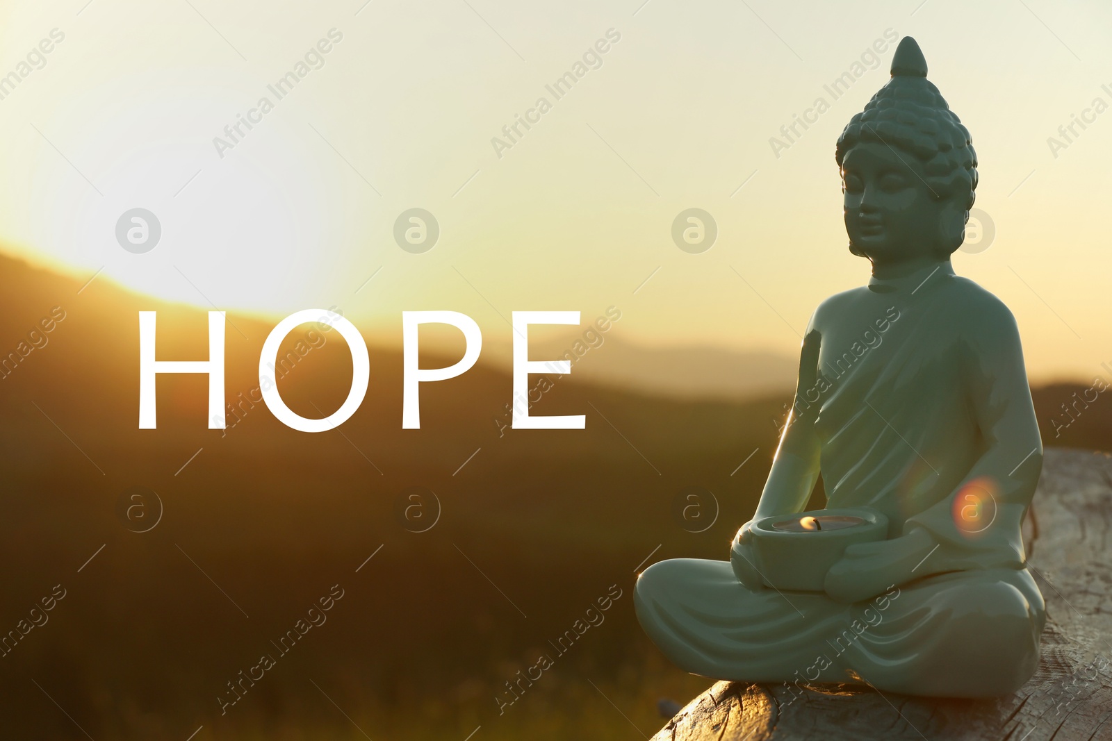 Image of Hope. Decorative Buddha statue with burning candle on log in mountains at sunrise