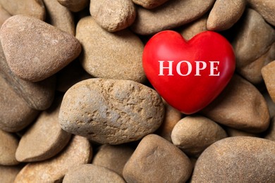 Image of Red decorative heart with word Hope on stones, top view