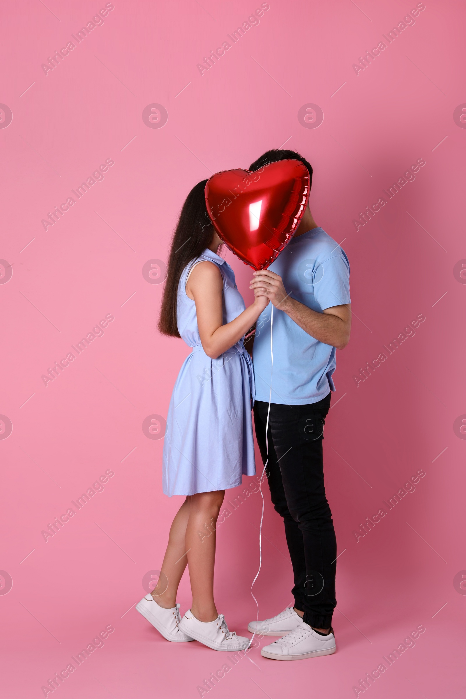 Photo of Lovely couple hiding behind heart shaped balloon on pink background. Valentine's day celebration