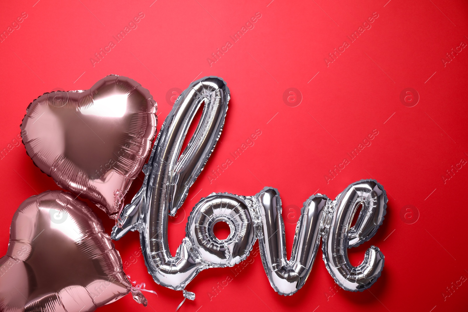 Photo of LOVE word and heart balloons on red background, flat lay