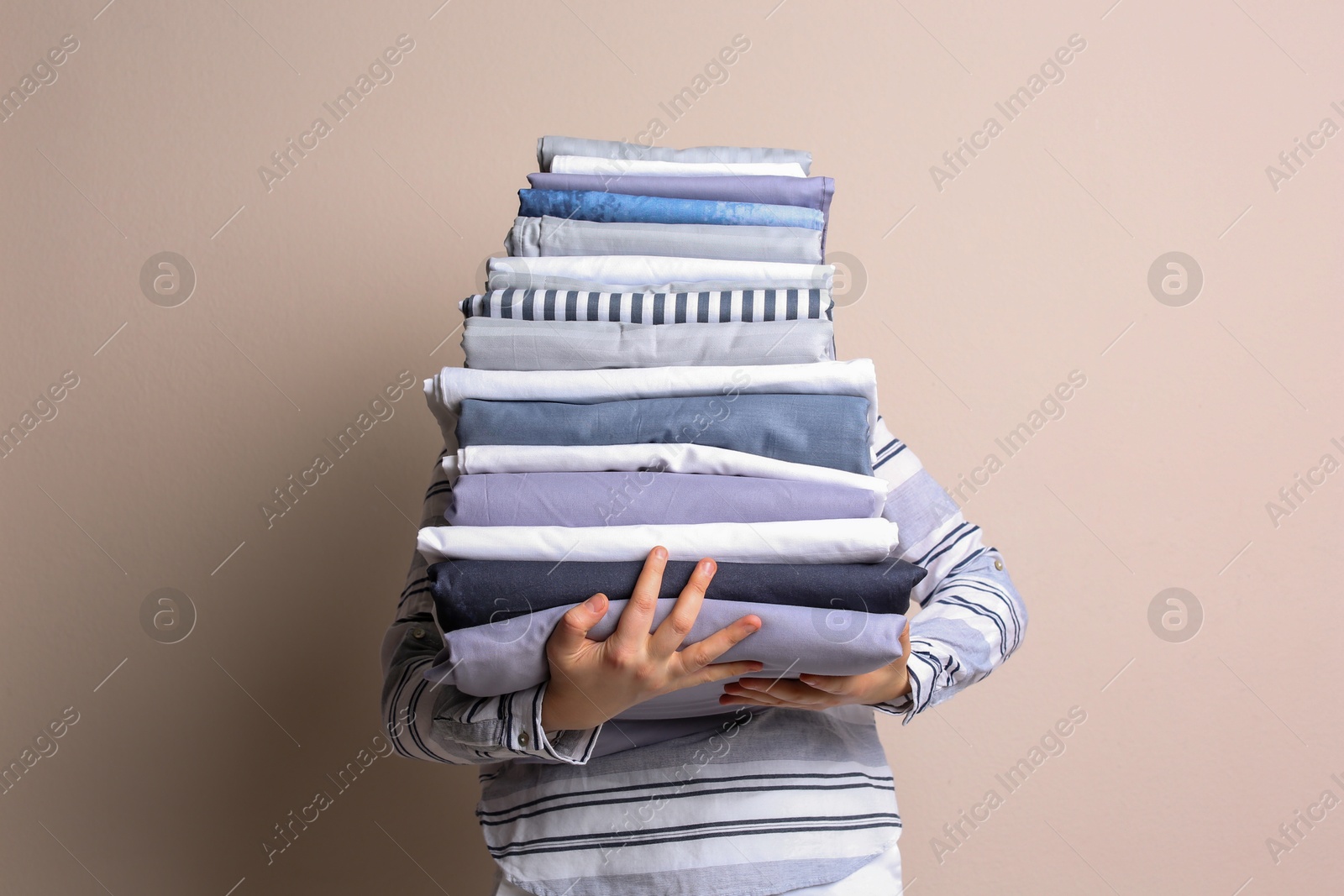 Photo of Woman holding stack of clean bed linens on beige background