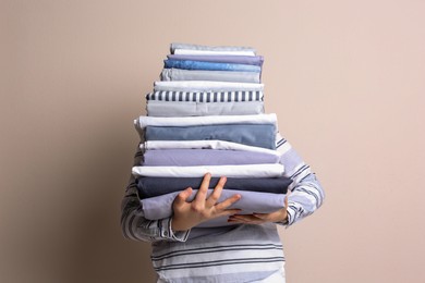 Woman holding stack of clean bed linens on beige background