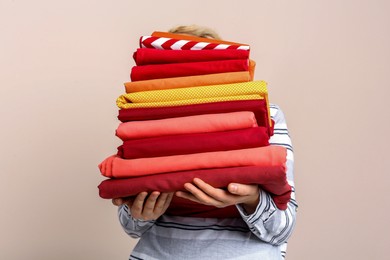 Photo of Woman holding stack of clean bed linens on beige background