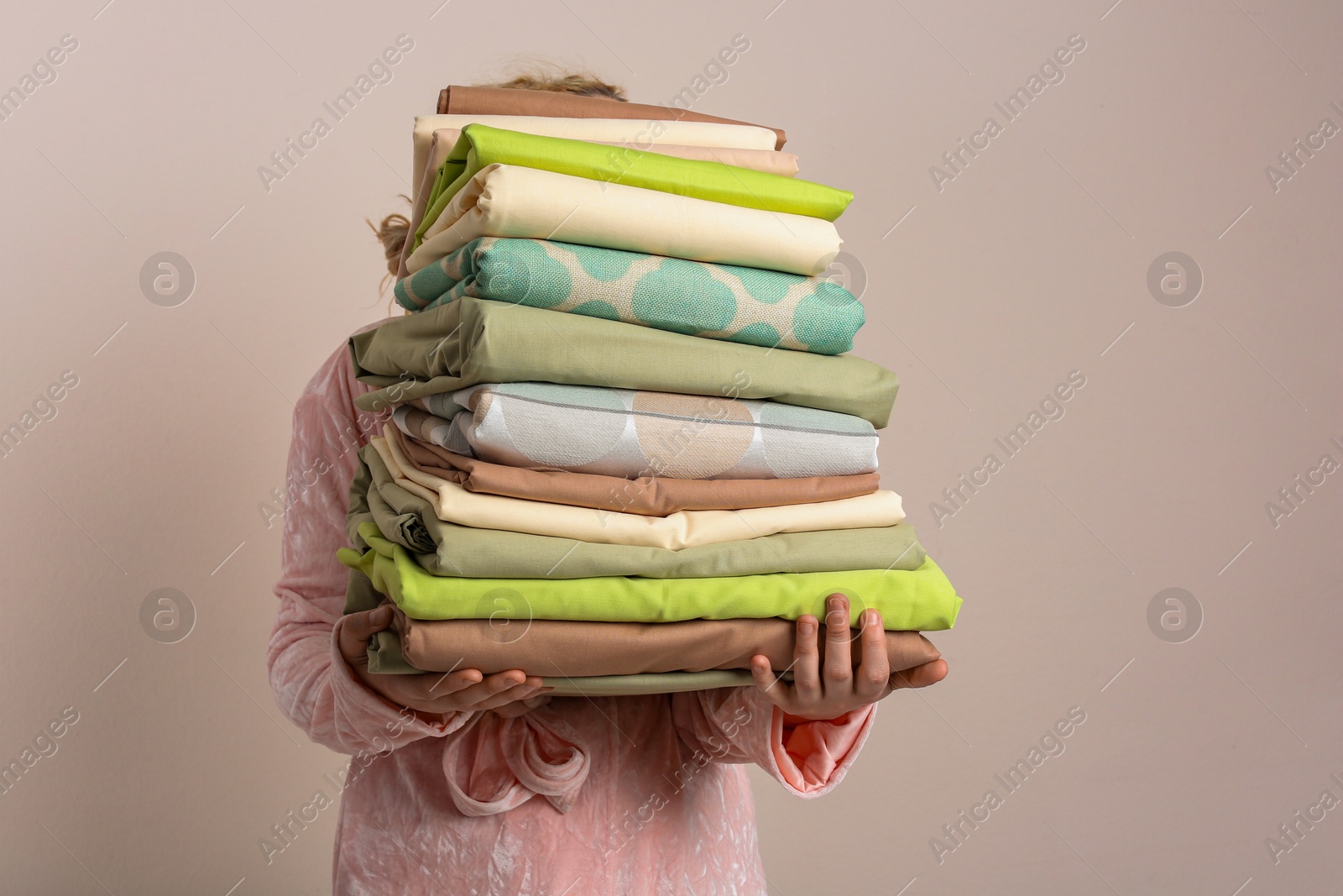 Photo of Woman holding stack of clean bed linens on beige background