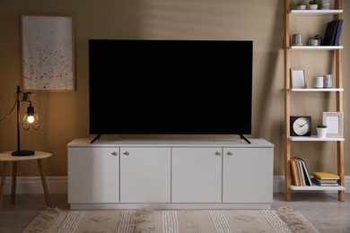 Photo of Modern TV on cabinet, white table and shelving unit near beige wall in room. Interior design