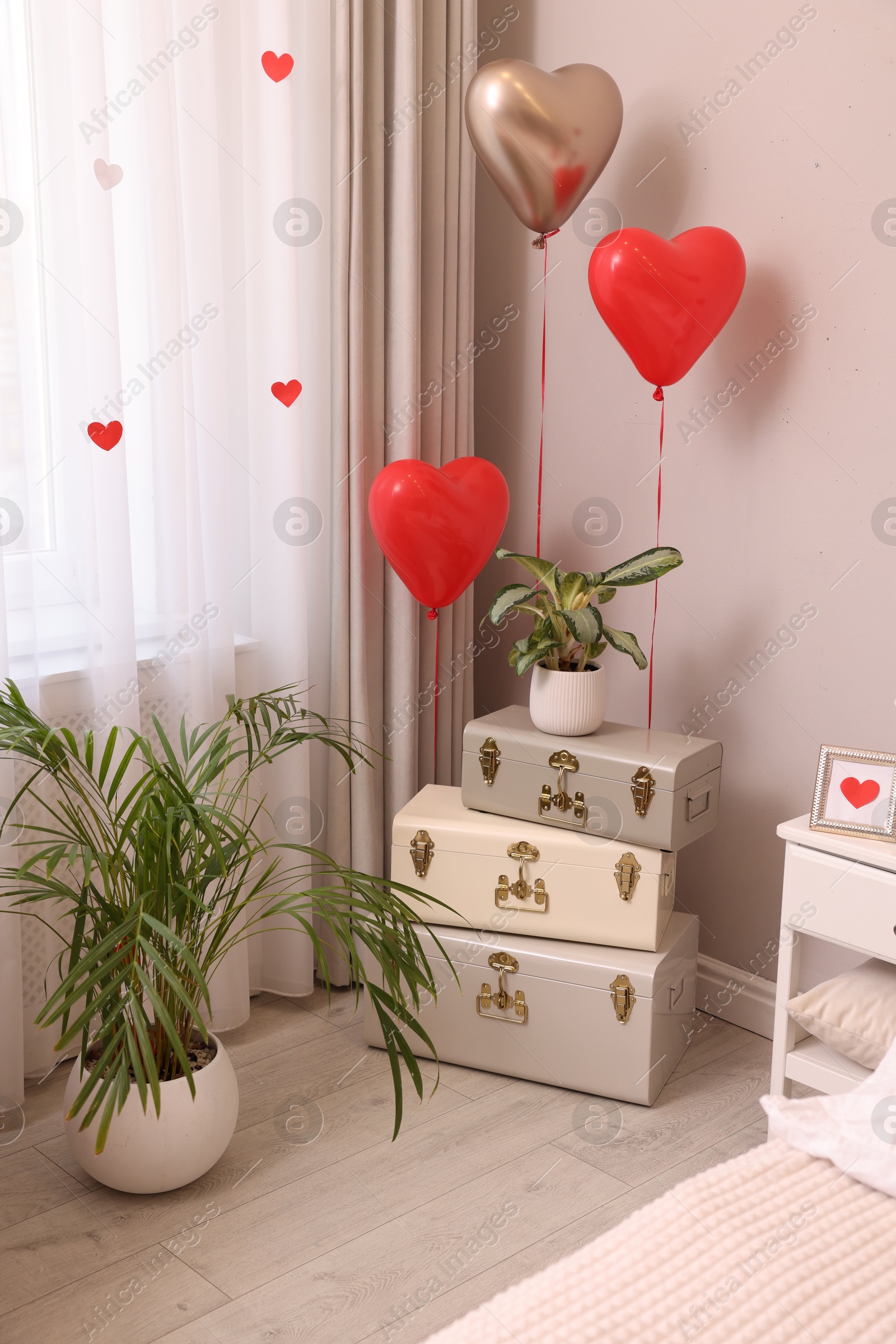 Photo of Cozy bedroom interior with heart shaped balloons and storage trunks near window. Valentine Day celebration