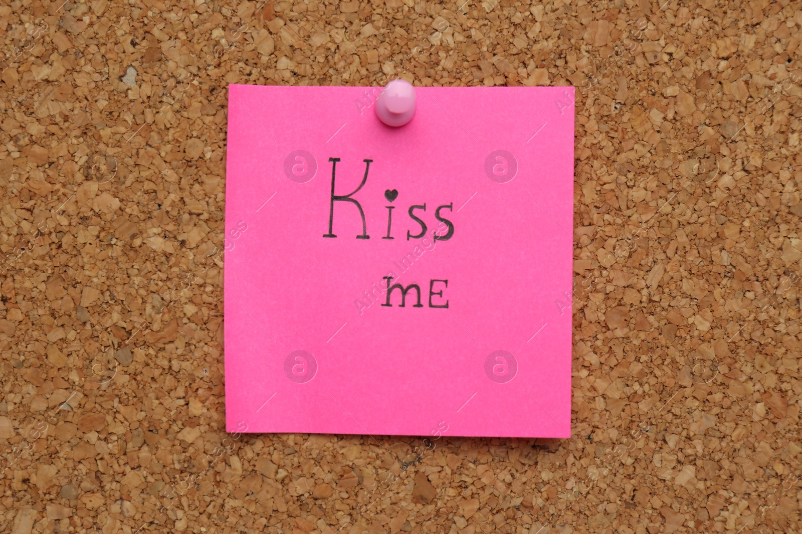 Photo of Pink paper note with phrase Kiss Me pinned to cork board