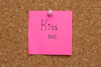 Photo of Pink paper note with phrase Kiss Me pinned to cork board