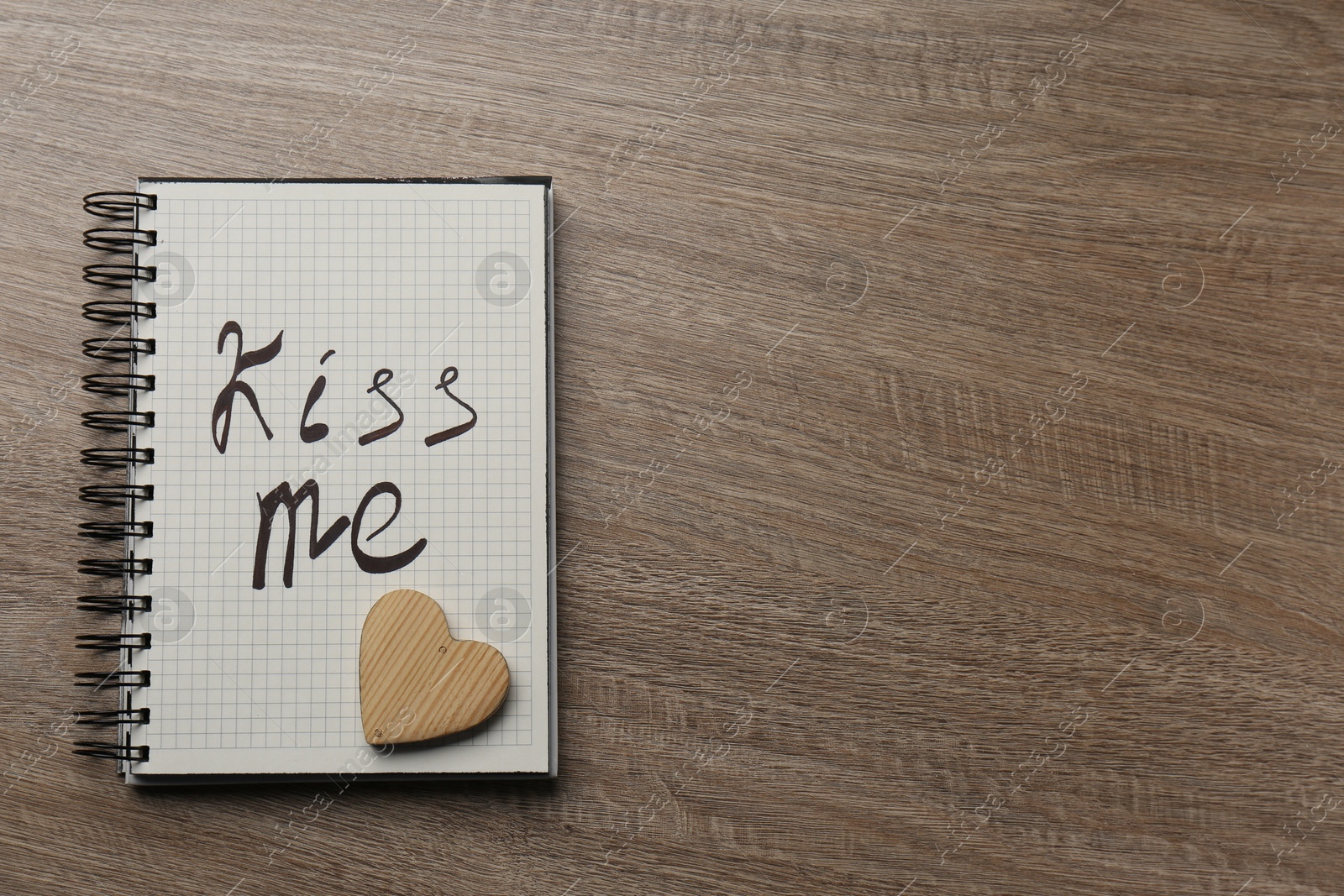 Photo of Notebook with phrase Kiss Me and decorative heart on wooden table, top view. Space for text