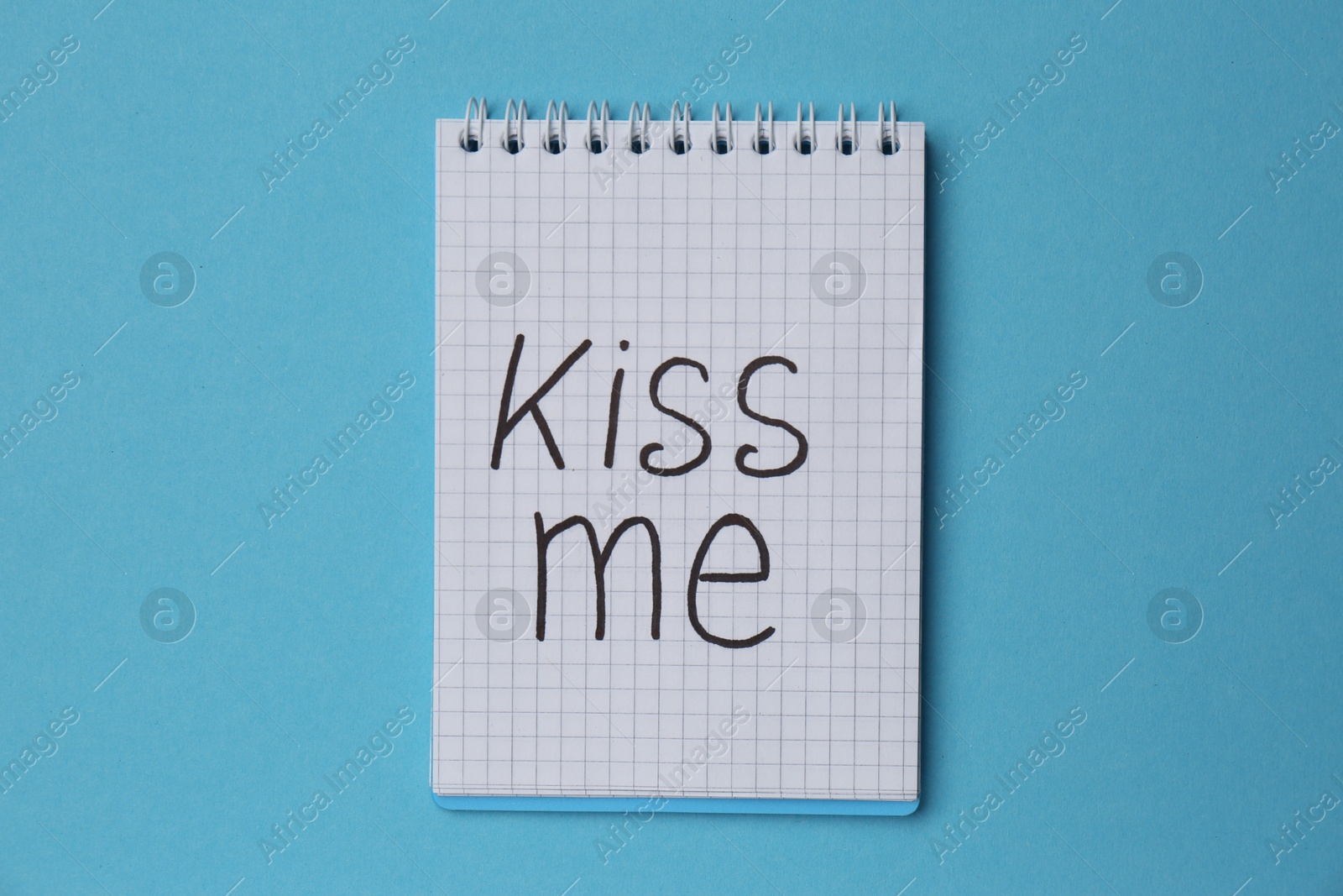 Photo of Notebook with phrase Kiss me on light blue background, top view