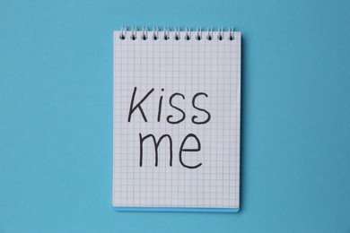 Photo of Notebook with phrase Kiss me on light blue background, top view