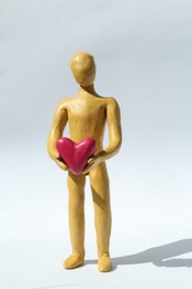 Photo of Yellow plasticine human figure with pink heart on white background