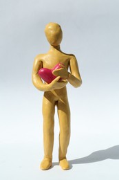 Photo of Yellow plasticine human figure with pink heart on white background