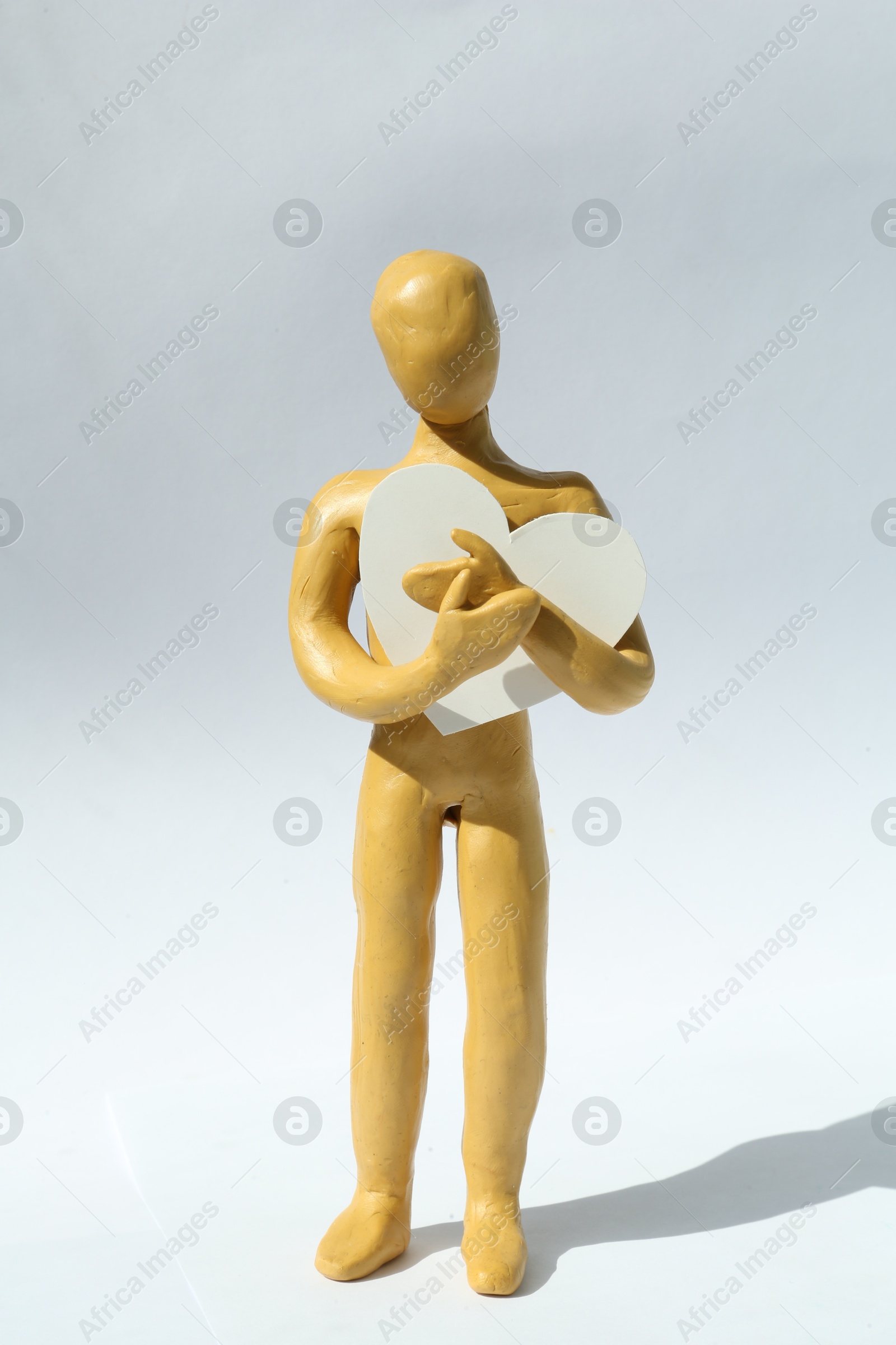 Photo of Yellow plasticine human figure with paper heart on white background