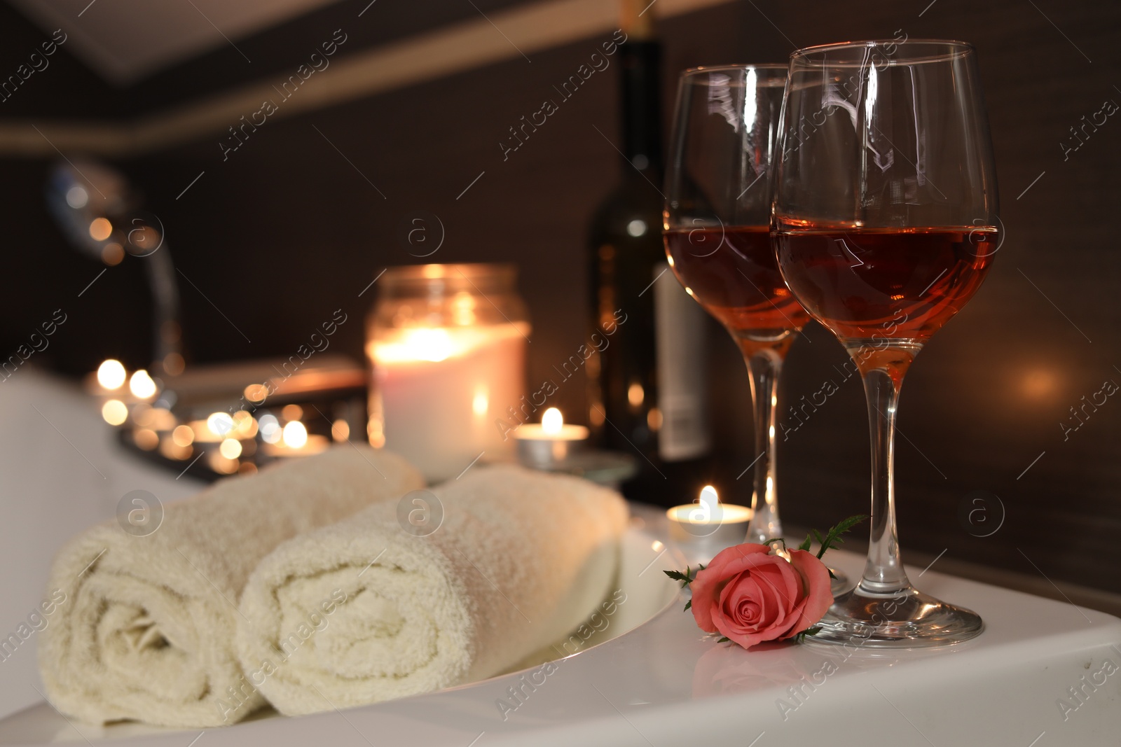 Photo of Glasses of wine, towels and rose on tub in bathroom, space for text. Romantic atmosphere