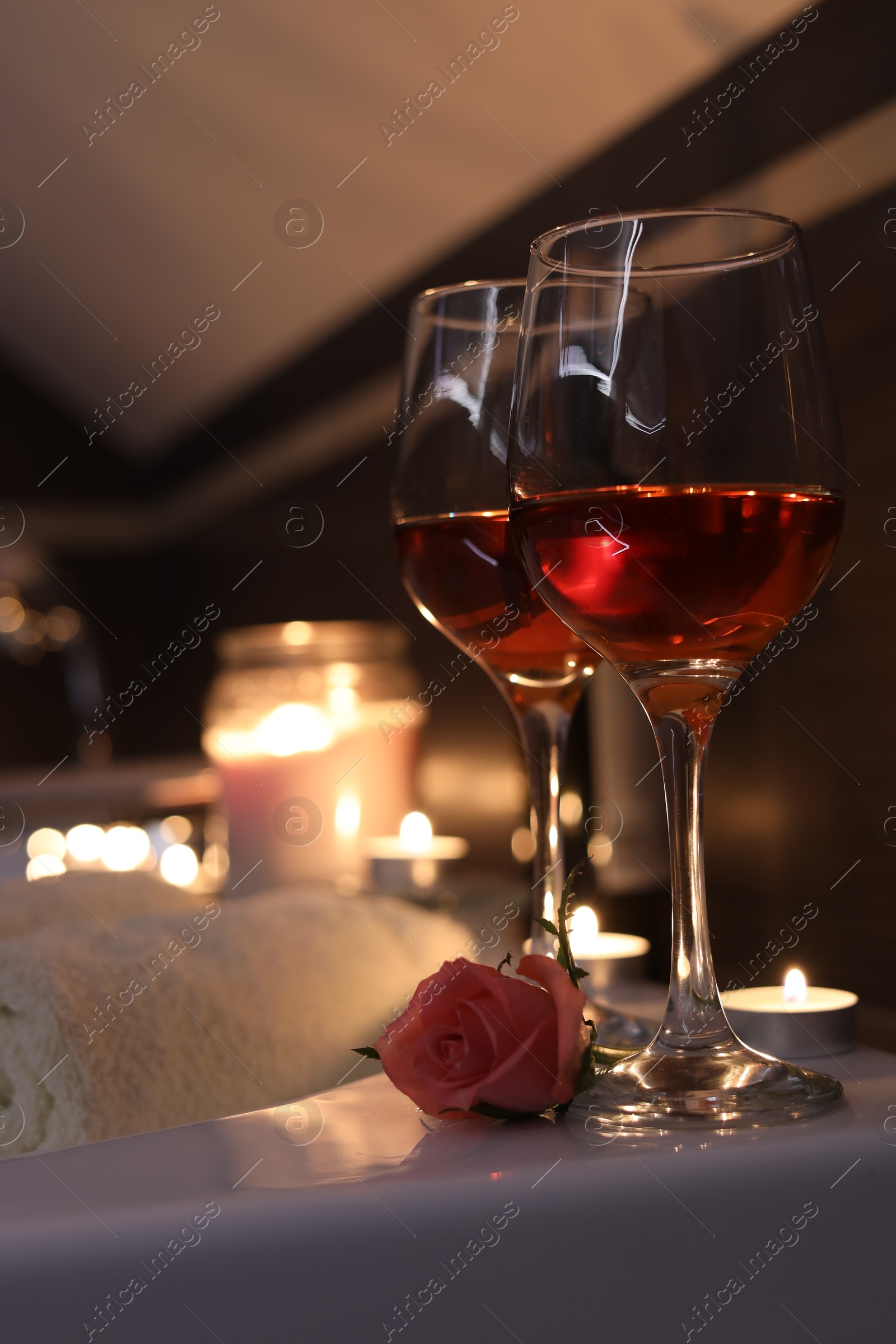 Photo of Glasses of wine and rose on tub in bathroom. Romantic atmosphere