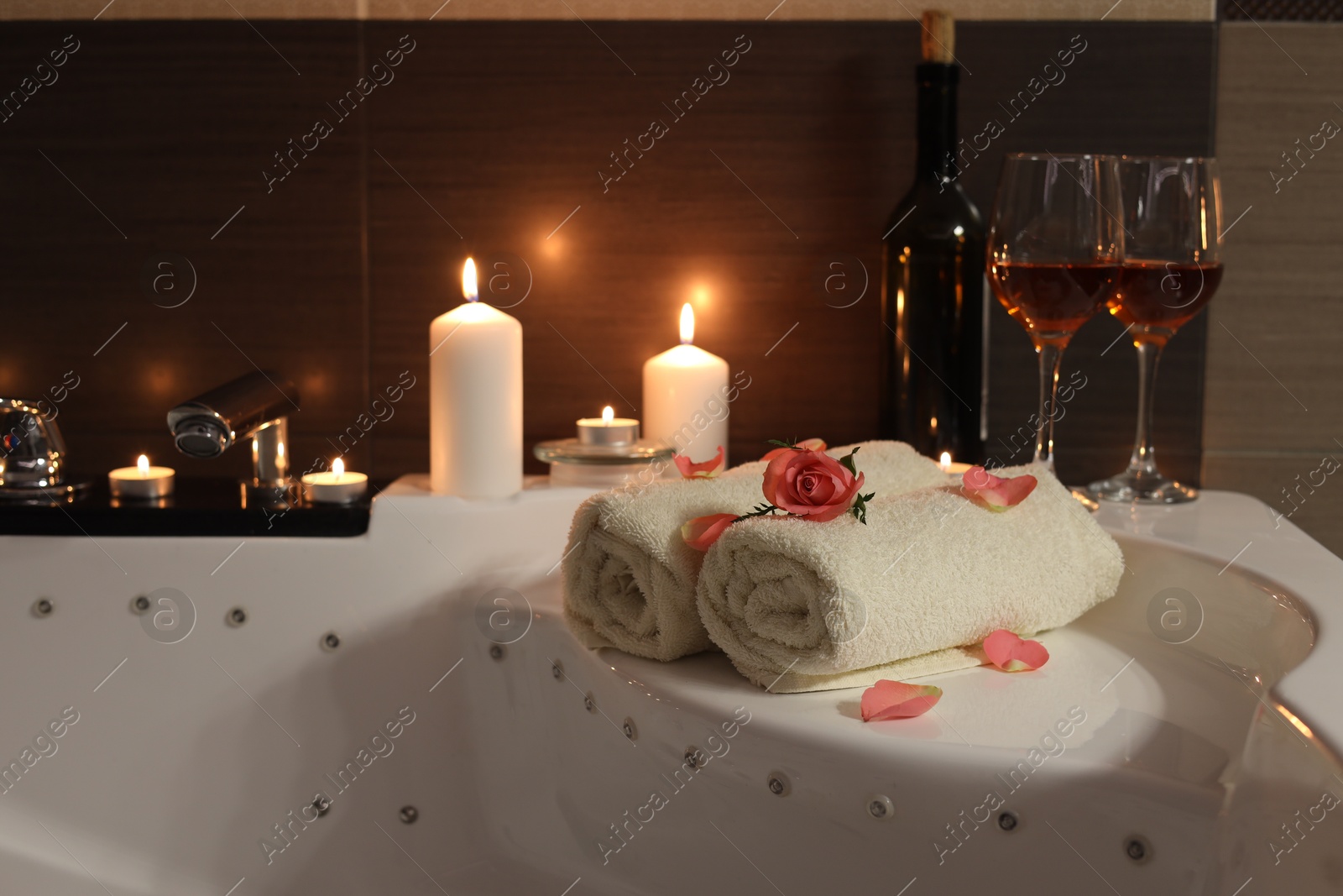 Photo of Glasses of wine, towels, candles and rose on tub in bathroom. Romantic atmosphere