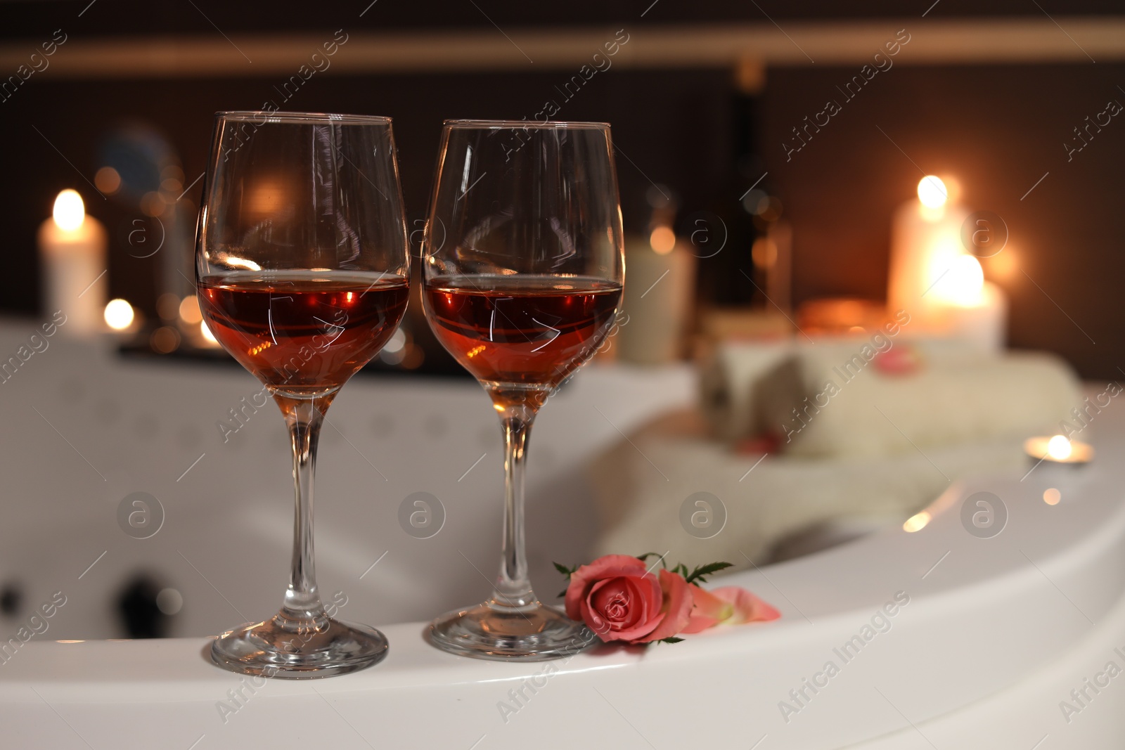 Photo of Wine in glasses and rose on edge of bath indoors. Romantic atmosphere