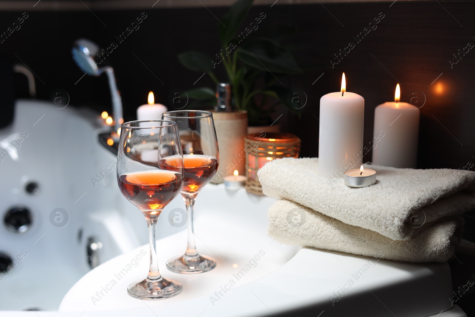 Photo of Bathtub with glasses of wine and candles indoors. Romantic atmosphere