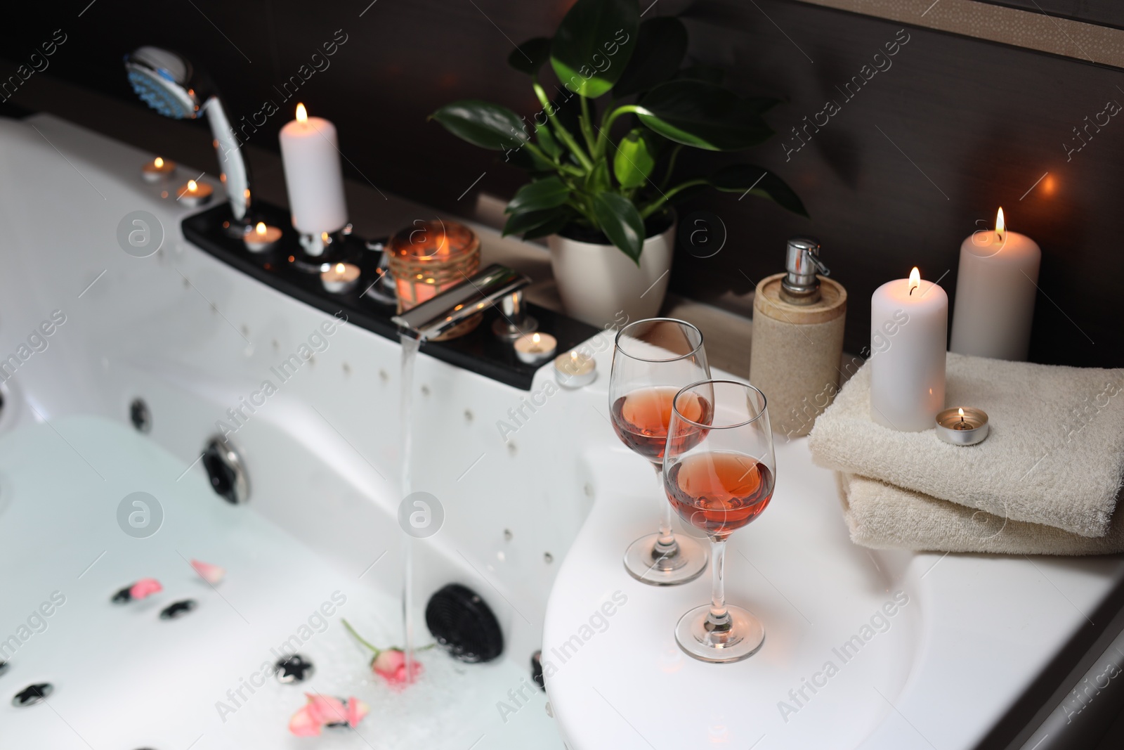 Photo of Bathtub with glasses of wine and candles indoors. Romantic atmosphere