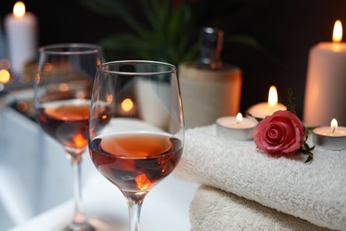 Photo of Wine in glasses and rose on edge of bath indoors, closeup. Romantic atmosphere