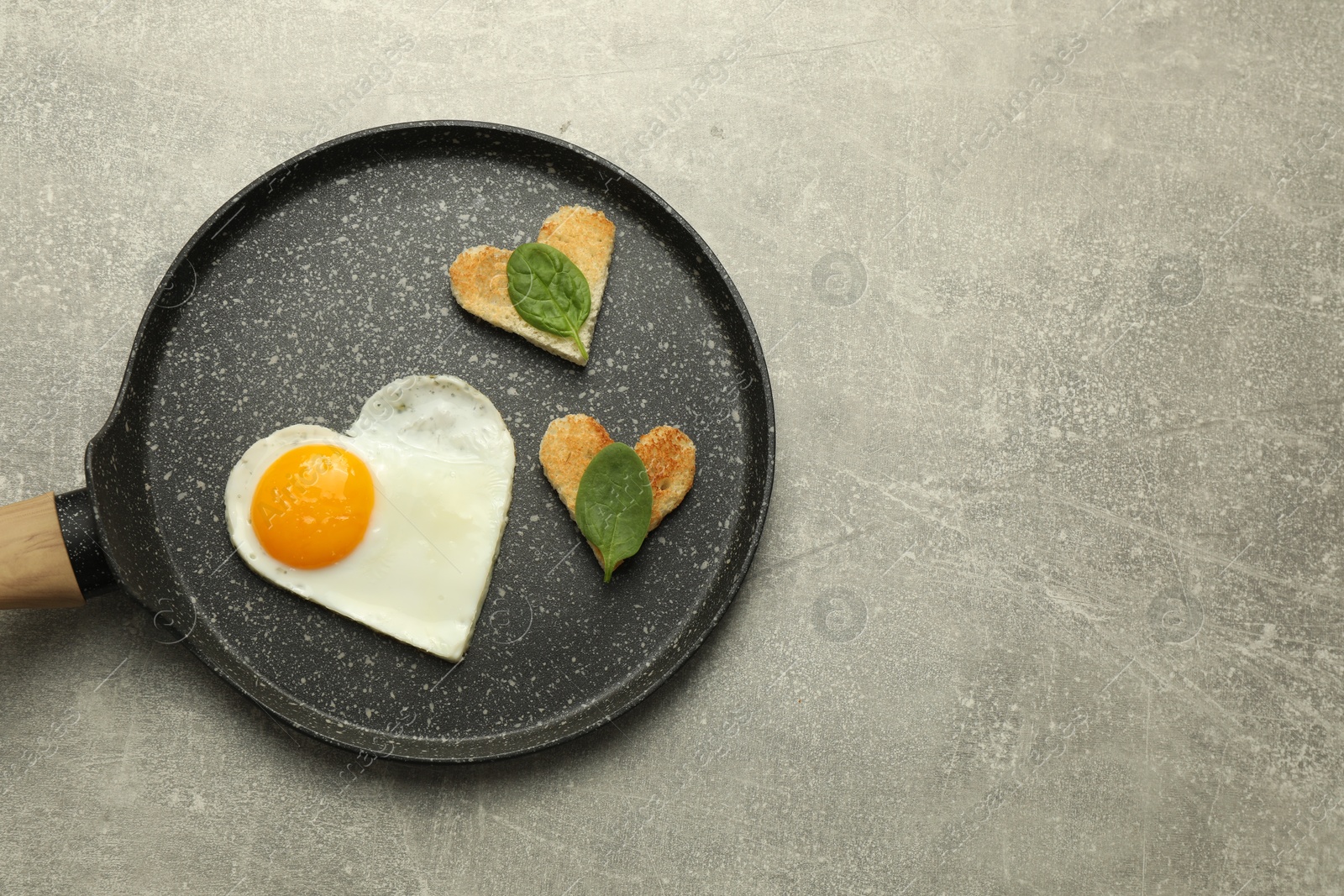 Photo of Heart shaped fried egg and toasts in frying pan on grey marble table, top view. Space for text