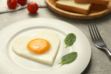 Photo of Heart shaped fried egg served on grey marble table, closeup