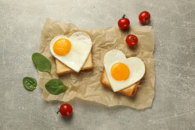 Photo of Heart shaped fried eggs with toasts, basil and tomatoes on marble table, flat lay