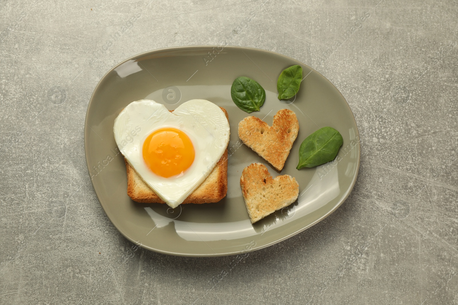 Photo of Heart shaped fried egg and toasts on grey marble table, top view