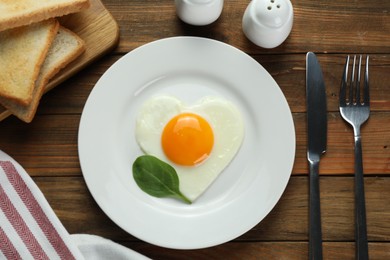 Photo of Romantic breakfast with heart shaped fried egg served on wooden table, flat lay