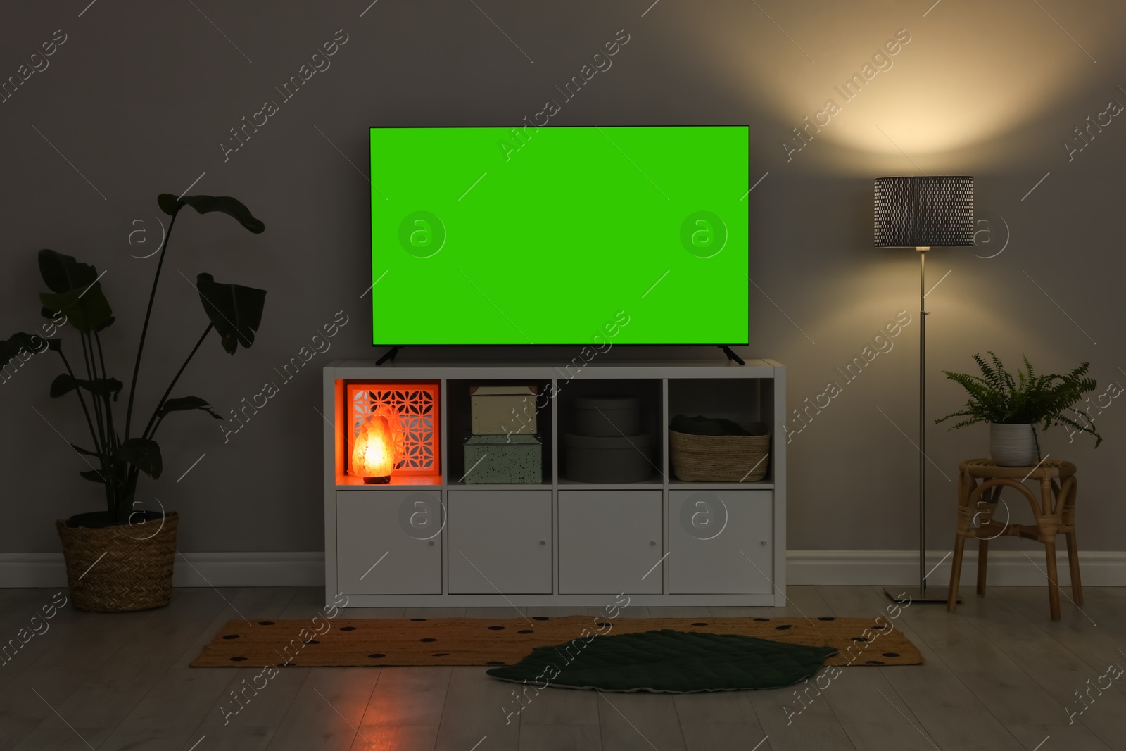 Photo of Modern TV on cabinet, lamp and beautiful houseplants near light wall indoors. Interior design