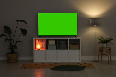 Photo of Modern TV on cabinet, lamp and beautiful houseplants near light wall indoors. Interior design