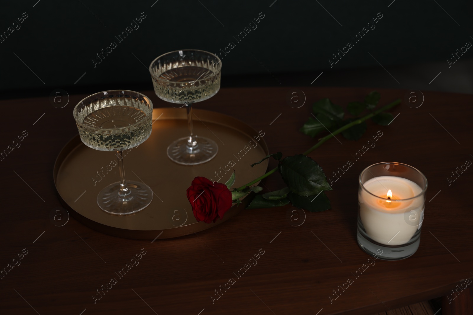 Photo of Burning candle, glasses of wine and beautiful red rose on wooden table indoors