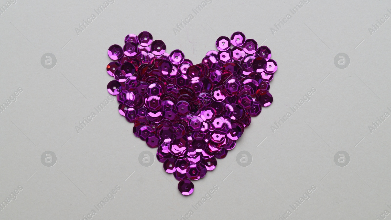 Photo of Purple sequins in shape of heart on light grey background, flat lay