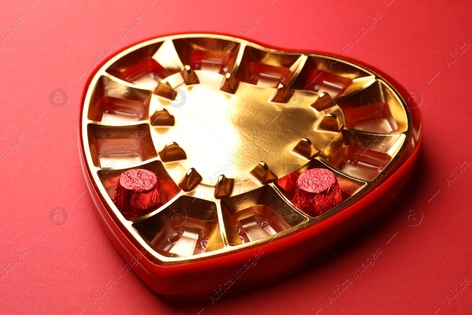 Photo of Partially empty heart shaped box of chocolate candies on red background