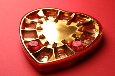 Photo of Partially empty heart shaped box of chocolate candies on red background