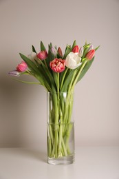 Photo of Beautiful bouquet of colorful tulips in glass vase on beige background