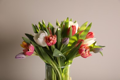 Photo of Beautiful bouquet of colorful tulips in glass vase on beige background