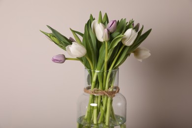 Photo of Beautiful bouquet of colorful tulips in glass vase on beige background