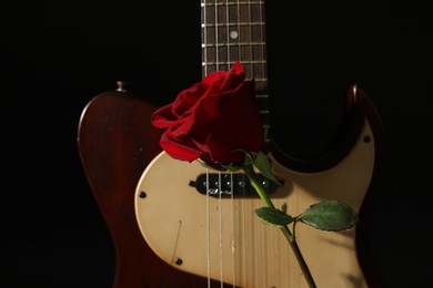 Photo of Beautiful rose near electric guitar on black background, closeup