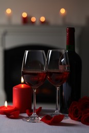 Photo of Romantic table setting with glasses of red wine, burning candles and rose flowers on grey table against blurred lights, space for text