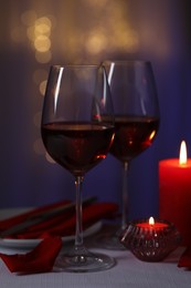 Photo of Romantic table setting with glasses of red wine and burning candles on grey table against blurred lights