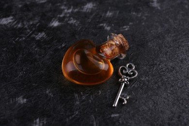 Photo of Heart shaped bottle of love potion with small key on black textured table