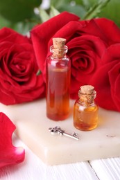 Photo of Bottles of love potion, red rose flowers and small key on white table, closeup