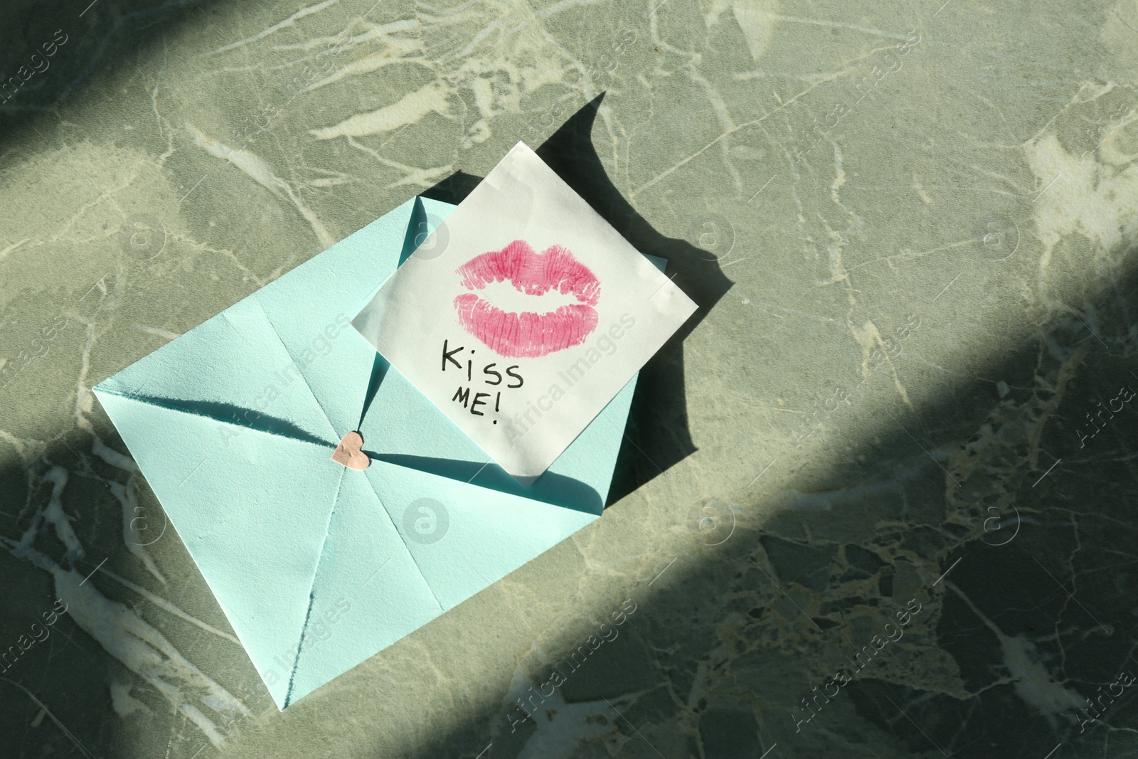 Note with phrase Kiss Me, lipstick mark and envelope on grey marble table, top view. Space for text Photo of Note with phrase Kiss Me, lipstick mark and envelope on grey marble table, top view. Space for text