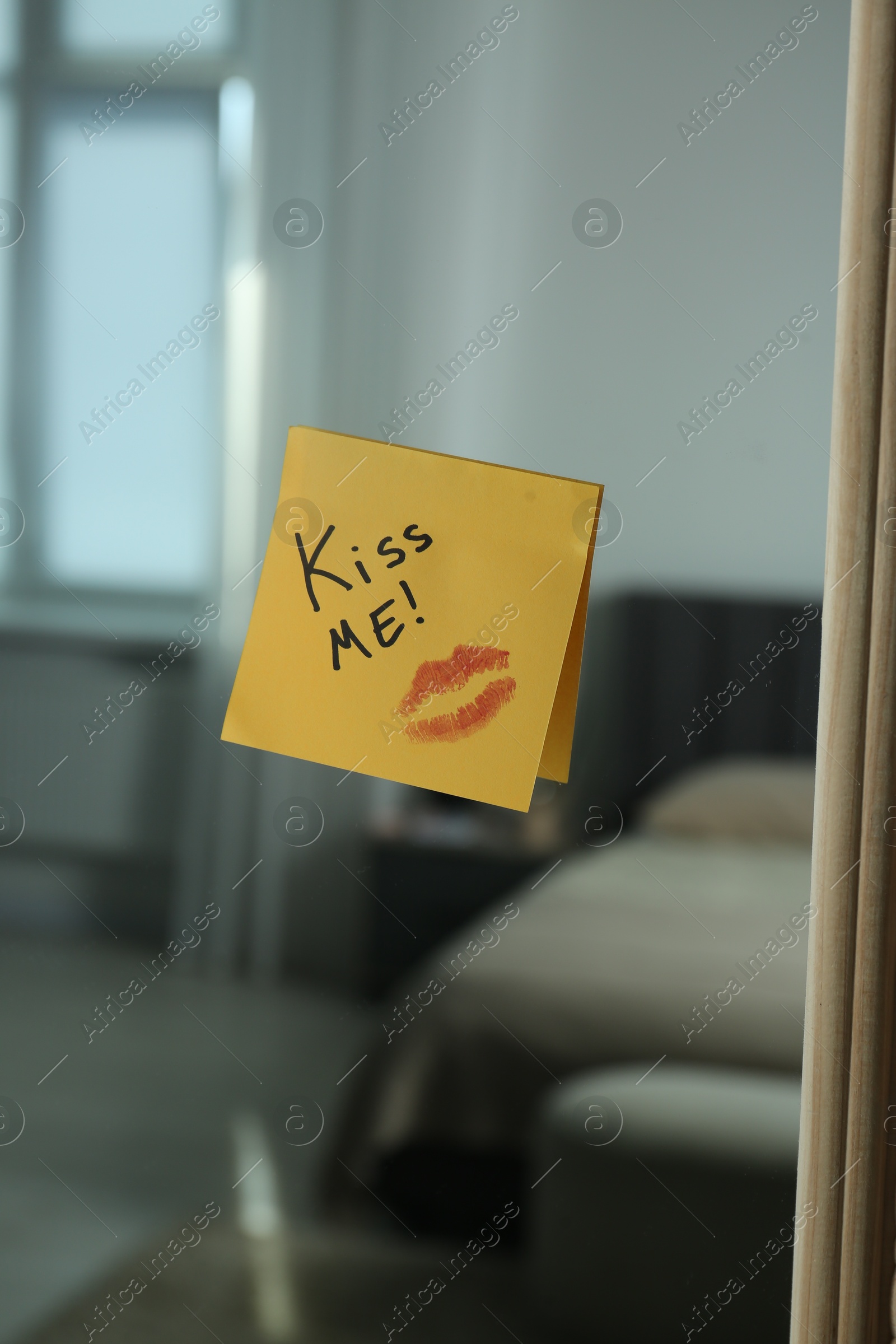 Sticky note with phrase Kiss Me and lipstick mark attached to mirror in room Photo of Sticky note with phrase Kiss Me and lipstick mark attached to mirror in room