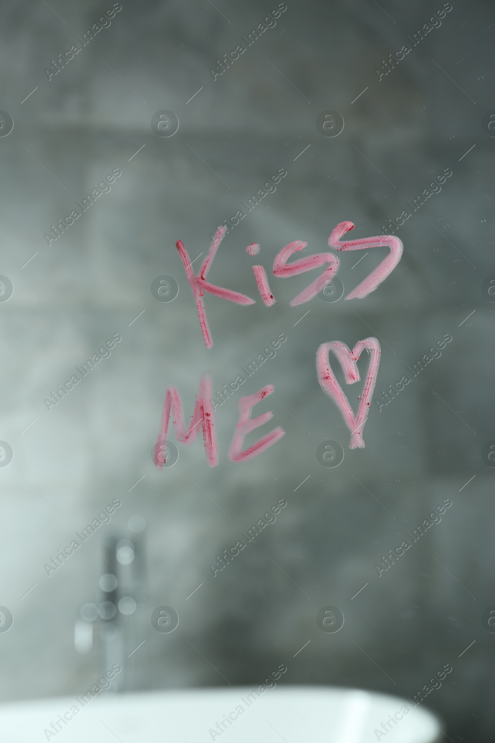 Red heart and phrase Kiss Me written with lipstick on mirror in bathroom Photo of Red heart and phrase Kiss Me written with lipstick on mirror in bathroom