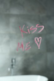 Photo of Red heart and phrase Kiss Me written with lipstick on mirror in bathroom